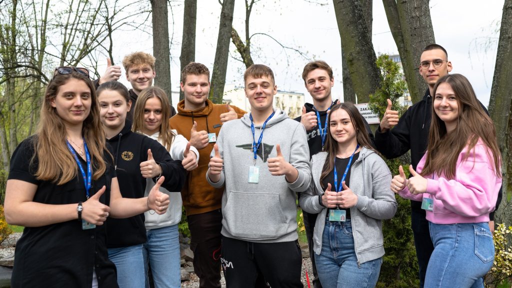 Grupa dziewczyn i chłopców stoi na dworze. Wszyscy pokazują kciuk w górę czyli okej.